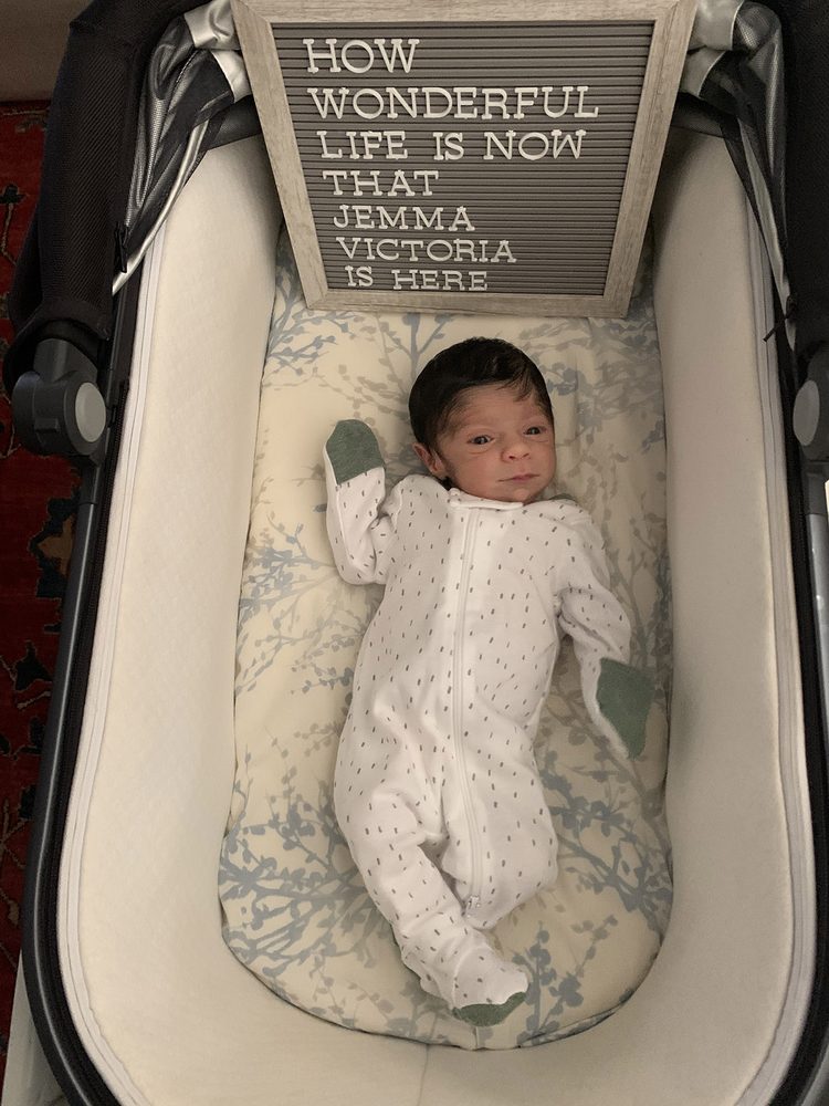 Baby Jemma in her bassinet beside a letterboard sign celebrating her arrival