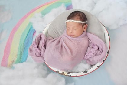 Sasha's newborn daughter swaddled in pink beside a rainbow