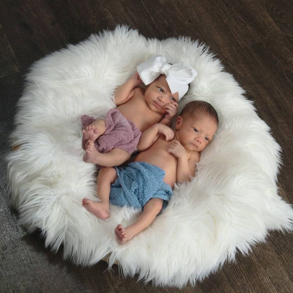 Elaine and Gio's newborn twins curled up together on a white fur blanket